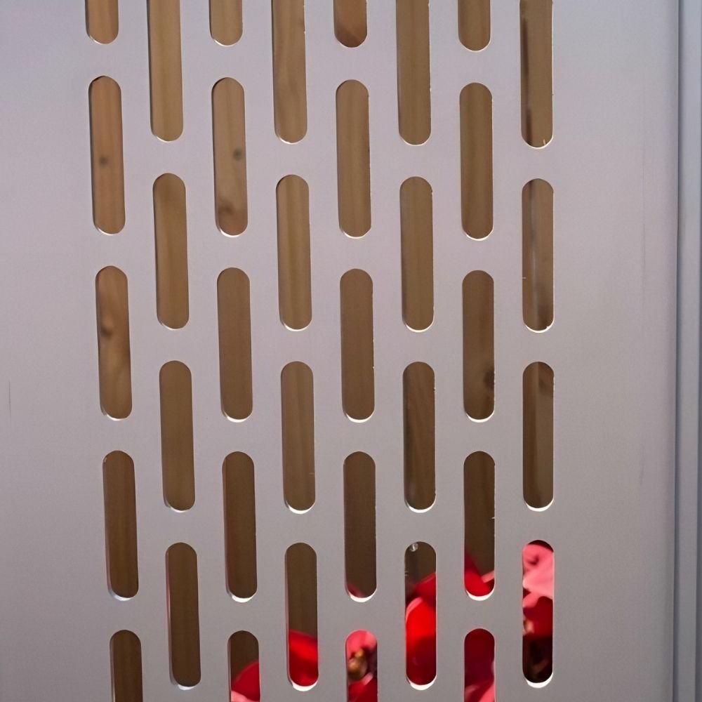 Un primer plano detallado de la cortina de aluminio troquelada Modelo Aíra, con el patrón de perforaciones oblongas en el primer plano. A través de las perforaciones, se revelan texturas rústicas de madera en el fondo, y una sola, vibrante flor roja es visible a través de una de las perforaciones individuales, añadiendo un contraste de color orgánico.