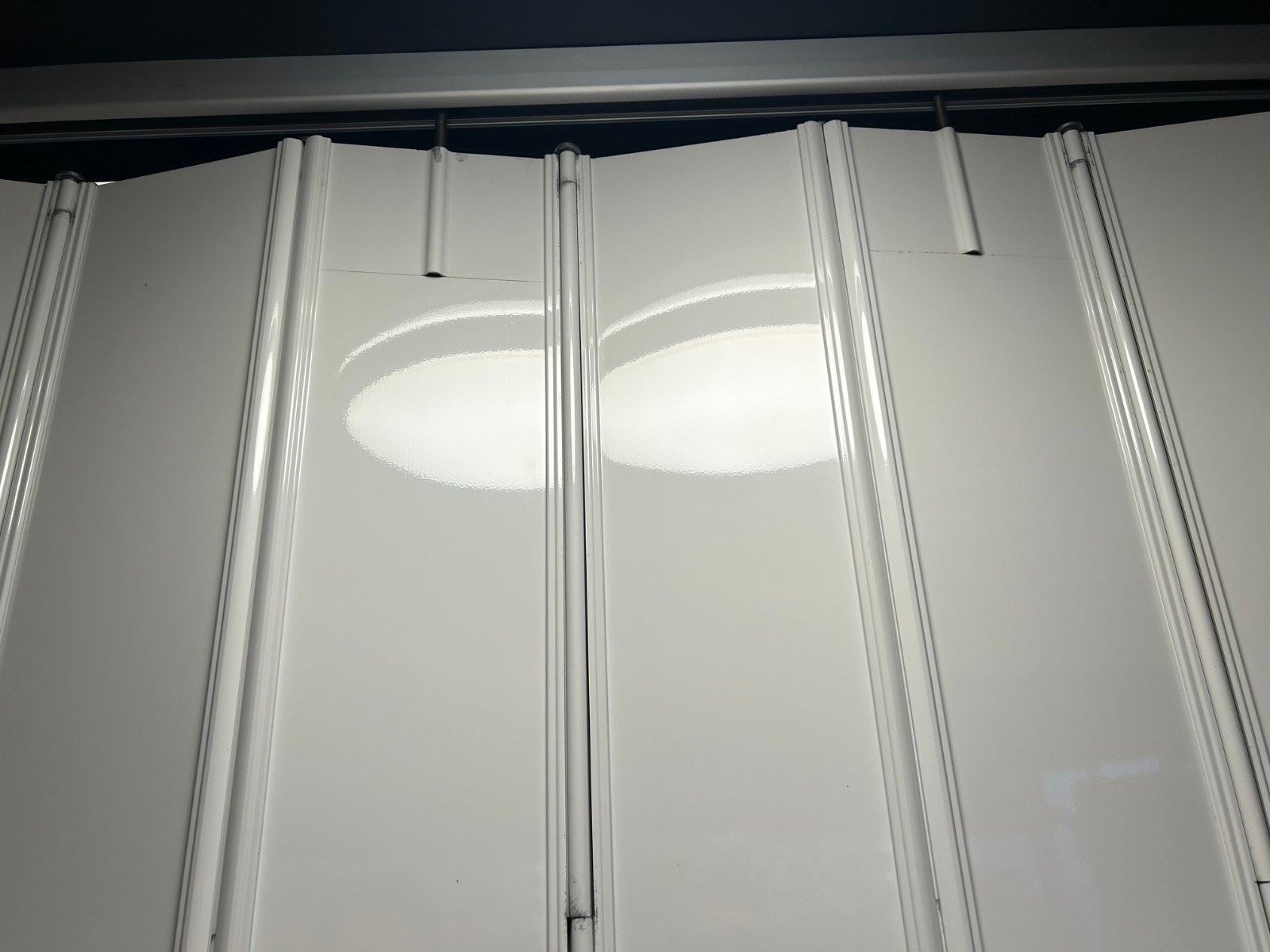 Vista en primer plano de la articulación superior de una cortina plegable blanca del Modelo Discreta, mostrando cómo la cortina de duela ciega se conecta al riel superior.